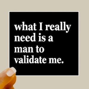 May include: A black square with white text that reads: "what I really need is a man to validate me." The square is held by a hand with a light beige background.