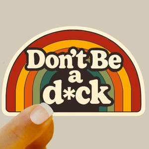 May include: A retro-style sticker with a rainbow design and the text "Don't Be a d*ck" in a bold, vintage font. The sticker has a cream-colored border and a neutral background.