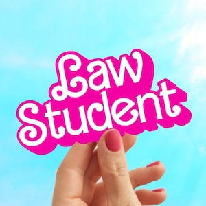 May include: A hand holds up a pink sign with the words "Law Student" in white letters against a blue sky.
