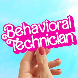 May include: A hand holds up a pink sign with the words "Behavioral Technician" in white letters.