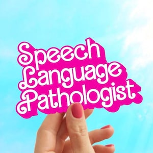 May include: A pink paper sign with the words "Speech Language Pathologist" written in white. The sign is being held up in front of a blue sky with white clouds.