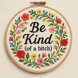 May include: A circular embroidery hoop featuring the phrase "Be Kind (of a bitch)" in black script. The text is encircled by a floral wreath of red, pink, yellow, and blue flowers with green foliage, set on a cream-colored fabric.