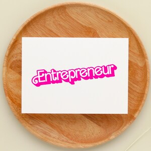 May include: A white card with the word "Entrepreneur" written in pink letters with a white outline on a wooden surface.