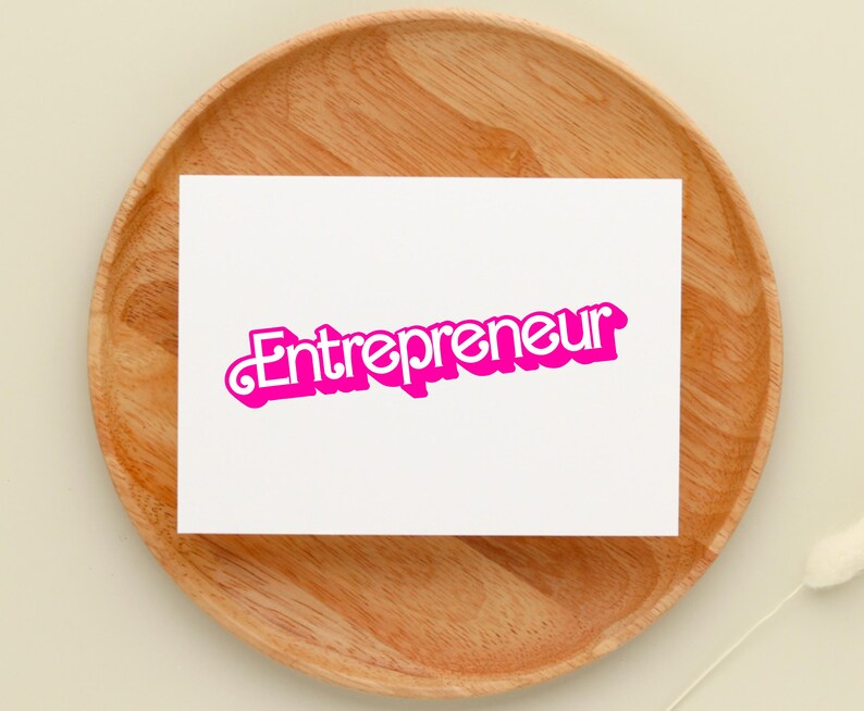 May include: A white card with the word "Entrepreneur" written in pink letters with a white outline on a wooden surface.