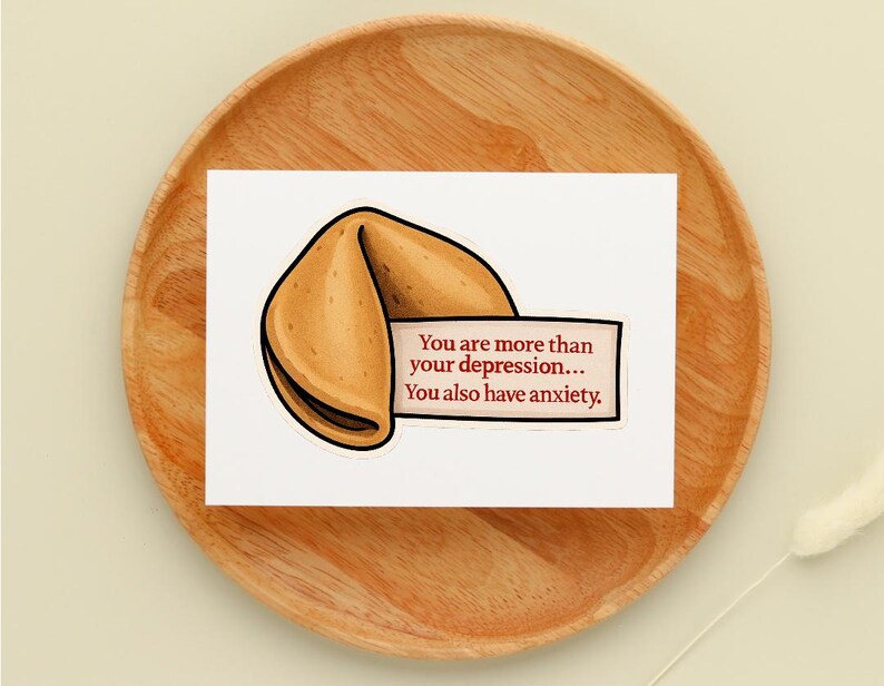 May include: A white card with a fortune cookie illustration and the text: "You are more than your depression... You also have anxiety." The card is on a wooden plate.