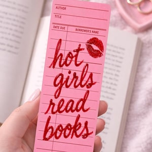 May include: Pink bookmark with the text "hot girls read books" in red script, along with a red lipstick kiss mark. The bookmark has lines for author, title, date due, and borrower's name.