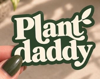 Op de afbeelding: Een gestanste sticker met de tekst Plant daddy in een vet, crèmekleurig schreeflettertype tegen een donker bosgroene achtergrond. Het ontwerp bevat een kleine bladgrafiek bevestigd aan de letter y, met een dikke groene rand.