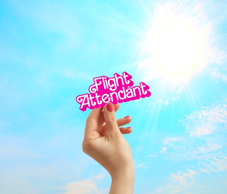 May include: A hand holds up a pink sign with the words "Flight Attendant" in white letters against a blue sky.