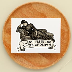 May include: A sticker featuring a vintage illustration of a woman reclining on a chaise lounge. The text on the banner reads, "I CAN'T, I'M IN THE DEPTHS OF DESPAIR." The sticker is placed on a wooden plate.