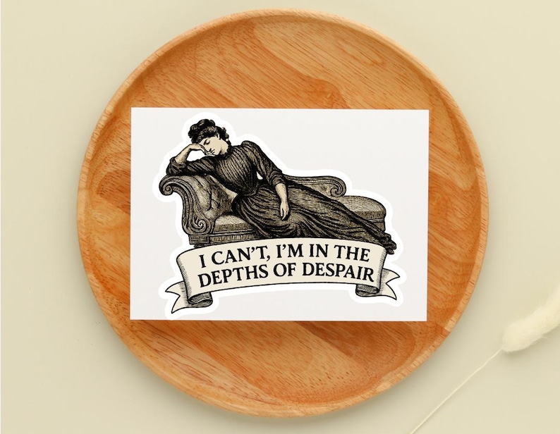 May include: A sticker featuring a vintage illustration of a woman reclining on a chaise lounge. The text on the banner reads, "I CAN'T, I'M IN THE DEPTHS OF DESPAIR." The sticker is placed on a wooden plate.
