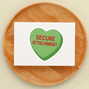 May include: A white card with a green heart-shaped graphic that reads "SECURE ATTACHMENT" in red text. The card is placed on a round, wooden plate.