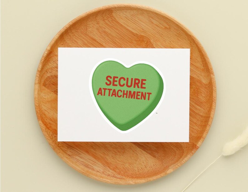 May include: A white card with a green heart-shaped graphic that reads "SECURE ATTACHMENT" in red text. The card is placed on a round, wooden plate.