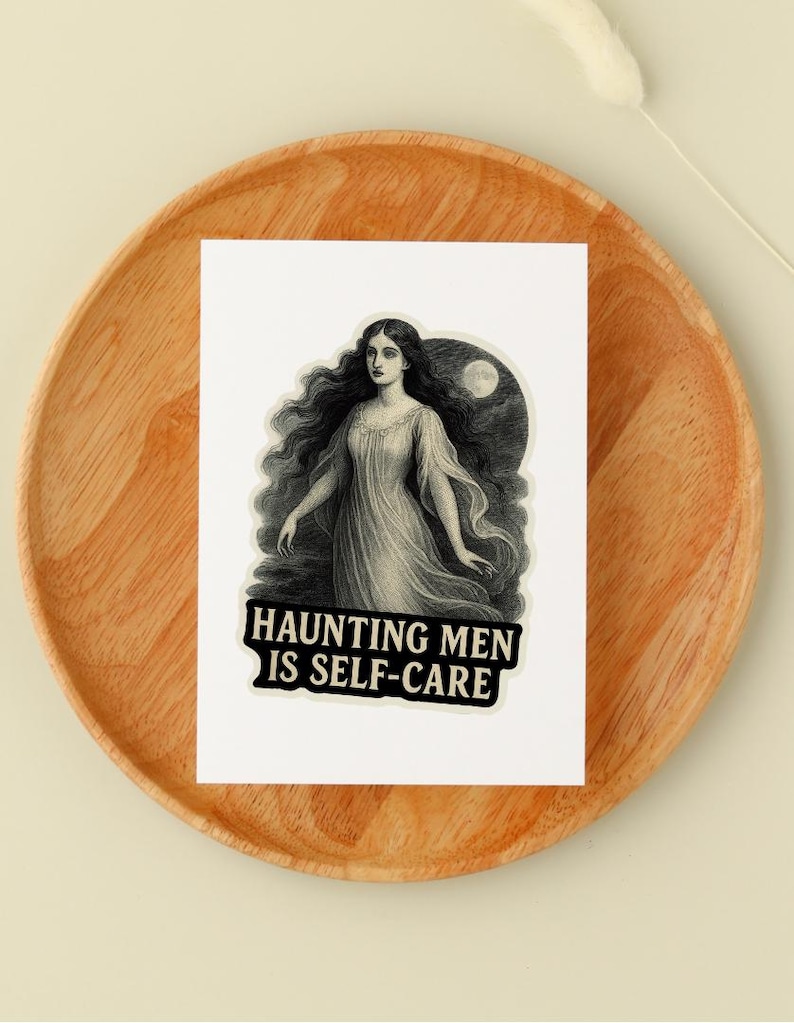 May include: A sticker featuring a vintage illustration of a woman with long, flowing hair and a flowing gown. The sticker has the text "Haunting Men Is Self-Care" in a bold, black font. The sticker is placed on a wooden plate.