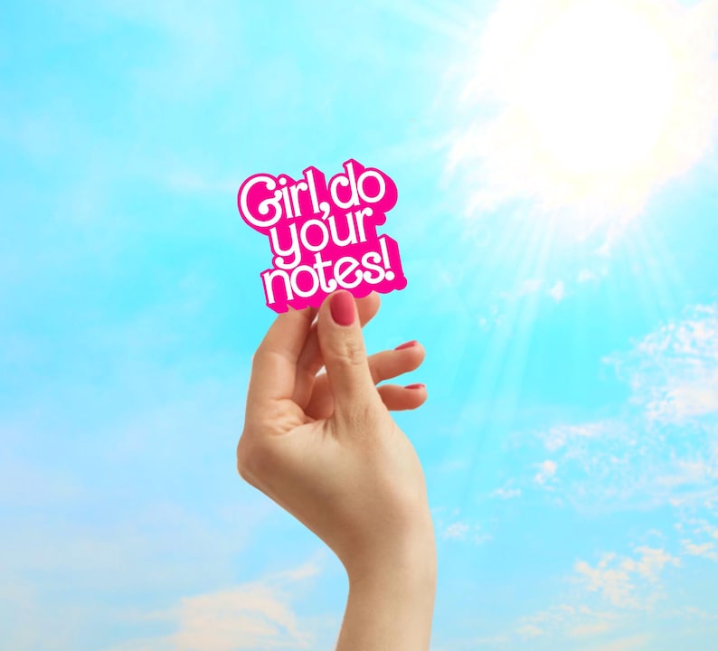 May include: A pink sticker with the text "Girl, do your notes!" is held up against a bright blue sky with sun rays. The sticker has a wavy outline and the text is in a playful font.