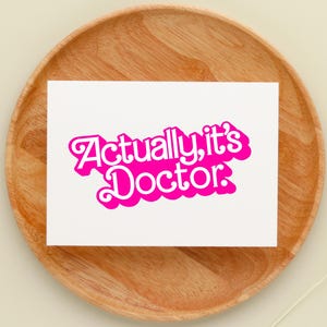 May include: A white card with the text "Actually, it's Doctor." in pink bubble letters.