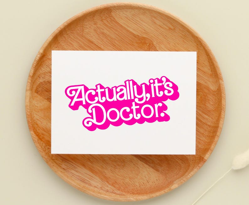 May include: A white card with the text "Actually, it's Doctor." in pink bubble letters.