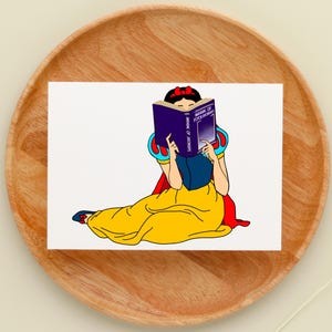 May include: A cartoon illustration of Snow White sitting and reading a book titled "Manual of Psychology". She is wearing a yellow dress with a red cape and a blue sash. The book is purple with gold lettering.