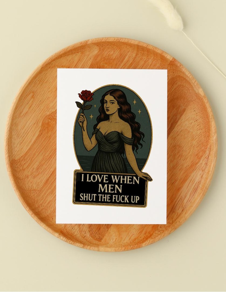 May include: A sticker featuring a woman holding a red rose, set against a teal background with stars. The text "I LOVE WHEN MEN SHUT THE FUCK UP" is displayed on a black banner below the illustration. The sticker is placed on a wooden plate.