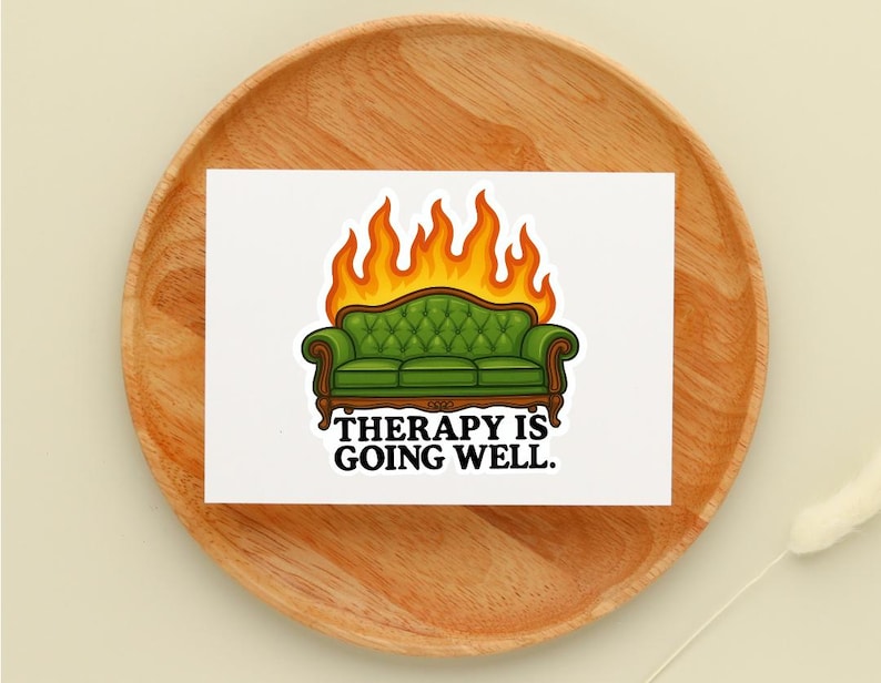 May include: A white sticker featuring a green couch engulfed in flames, with the text "THERAPY IS GOING WELL." The couch has a tufted back and wooden frame. The flames are orange and yellow.