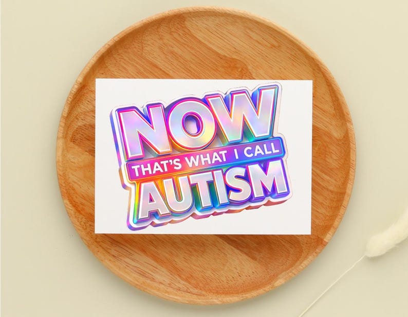 May include: A white card with the text "NOW THAT'S WHAT I CALL AUTISM" in a holographic, 3D-style font. The card is on a wooden plate, with a light beige background.