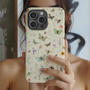 May include: A cream-colored phone case featuring a floral and insect design. The case is adorned with butterflies, bees, flowers, and other botanical elements in various colors. The phone case has a camera module with three lenses.