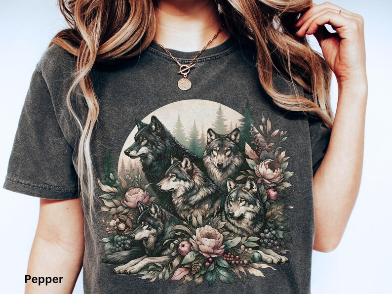 May include: A dark gray t-shirt with a graphic print of five wolves surrounded by flowers and greenery. The wolves are depicted in a realistic style with detailed fur and expressions.