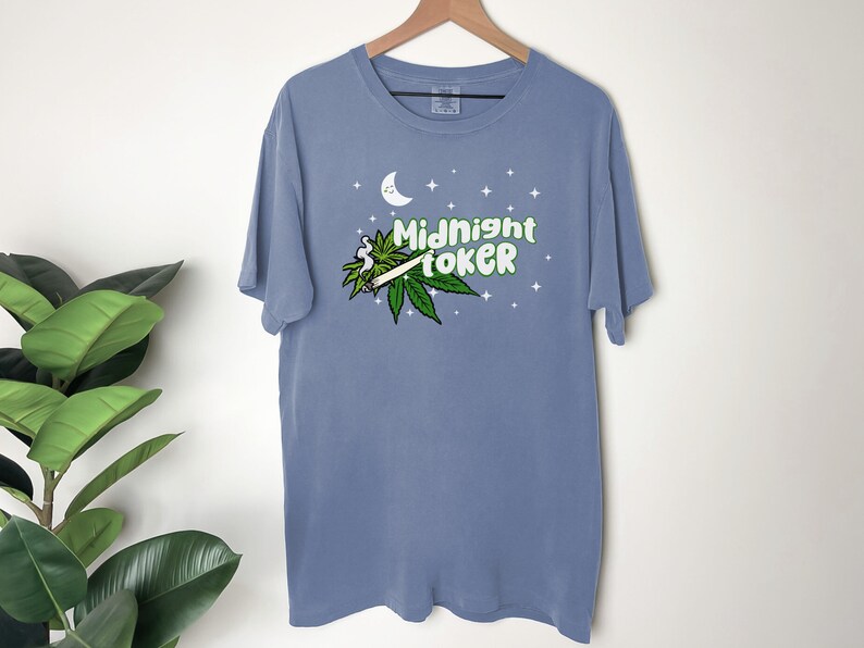 May include: A blue t-shirt with the words "Midnight Toker" in green and white, along with a cannabis leaf and a lit joint. The design includes a crescent moon and stars.