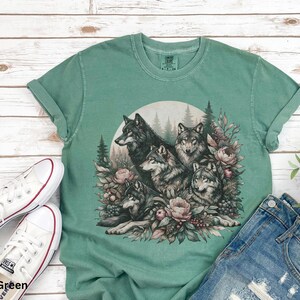 May include: A light green t-shirt with a graphic print of a group of wolves surrounded by flowers and foliage. The wolves are in shades of gray and brown, and the flowers are in shades of pink and purple.