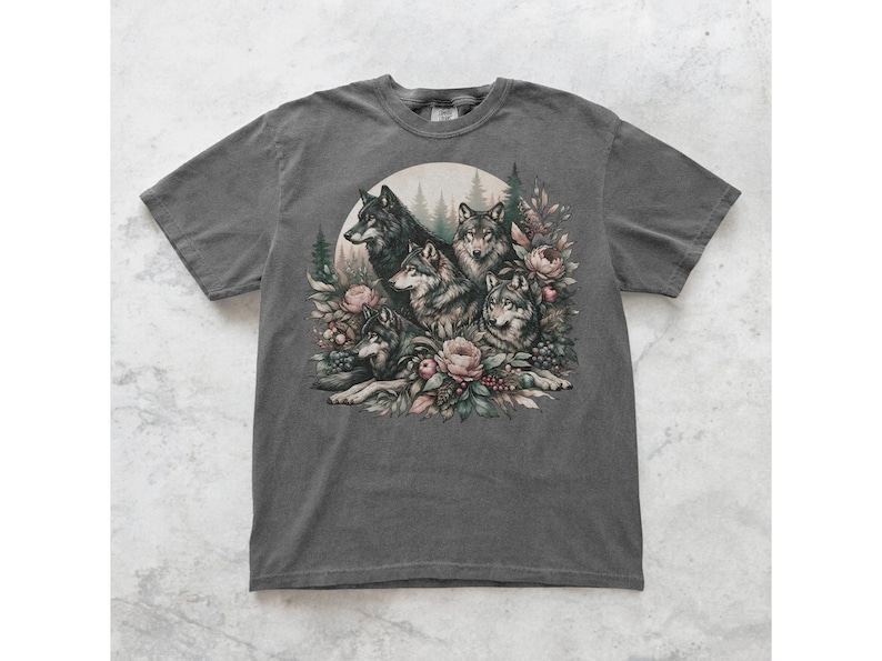 May include: A dark gray t-shirt with a graphic print of a group of wolves surrounded by flowers and foliage. The wolves are depicted in a realistic style with detailed fur and facial expressions.