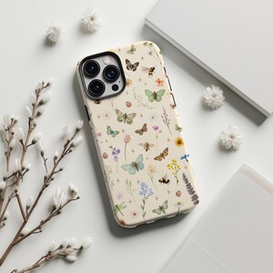 May include: A phone case with a cream-colored background, adorned with a pattern of colorful butterflies, bees, flowers, and other botanical elements. The case has a glossy finish and a camera cutout. The design is reminiscent of a spring garden.