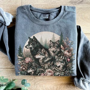 May include: A dark gray sweatshirt with a vintage-style print of five wolves surrounded by flowers and foliage. The wolves are in a circle, and the print has a faded, distressed look.