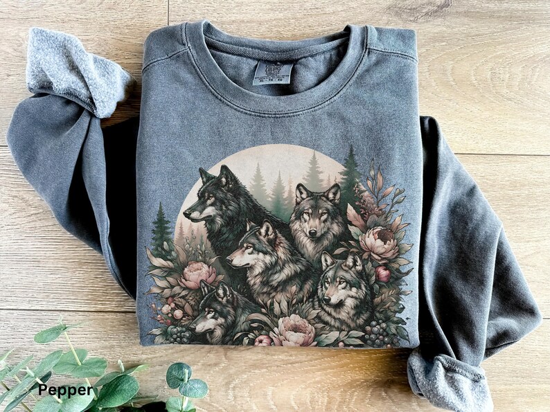 May include: A dark gray sweatshirt with a vintage-style print of five wolves surrounded by flowers and foliage. The wolves are in a circle, and the print has a faded, distressed look.