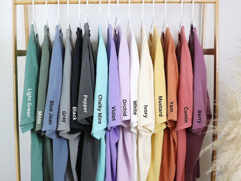 May include: A rack of 12 t-shirts in various colors, including light green, blue jean, gray, black, pepper, chalky mint, violet, orchid, white, ivory, mustard, yam, cumin, and berry.
