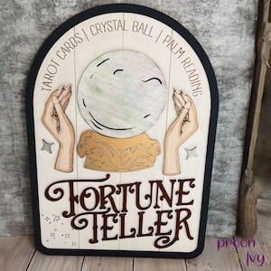 May include: A wooden sign with a fortune teller theme. It features a crystal ball, two hands, and the text "Tarot Cards | Crystal Ball | Palm Reading" and "Fortune Teller".