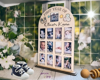 May include: A wooden photo frame with a cutout arch design. The frame has 12 spaces for photos, each labeled with a month of the year. The frame is personalized with the name "Oliver Kane" and the text "First Year Of".