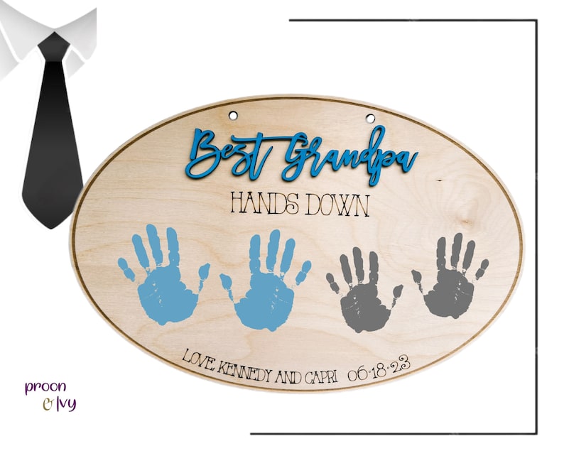 May include: Oval wooden sign with the text "Best Grandpa Hands Down" in black lettering.  The sign has three handprints, two in blue and one in gray, with the text "Love Kennedy and Capri 06-18-23" below the handprints.