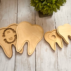 May include: Three wooden teeth shapes, one with a cutout of a heart and two with cutouts for upper and lower teeth. The teeth are made of light brown wood and are arranged on a light wood surface.