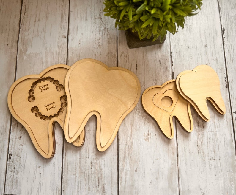 May include: Three wooden teeth shapes, one with a cutout of a heart and two with cutouts for upper and lower teeth. The teeth are made of light brown wood and are arranged on a light wood surface.