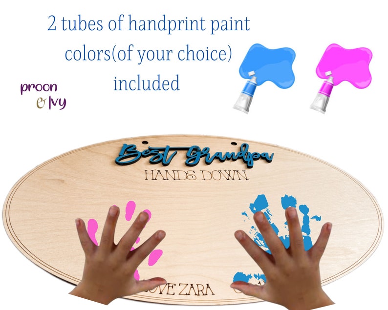 May include: Wooden oval sign with the text "Best Grandpa Hands Down" and space for two handprints. The sign is light brown and has a natural wood grain. Two tubes of paint are included, one blue and one pink.