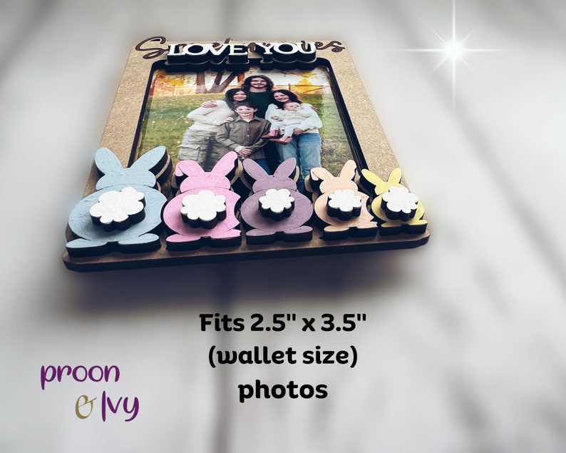 Peut inclure: Cadre photo en bois avec une photo de famille, orn&eacute; d'accents de lapins color&eacute;s. Le cadre est con&ccedil;u pour des photos de 6,35 cm x 8,89 cm et porte l'inscription "Love You" en haut. Le cadre pr&eacute;sente des queues de lapin bleues, roses, violettes, p&ecirc;che et jaunes.