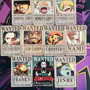 May include: A collection of eleven rectangular game cards featuring One Piece characters on Wanted posters. Each card displays the text WANTED, DEAD OR ALIVE, the character name, a bounty amount, and game instructions like Your Turn +1000 MARINE.