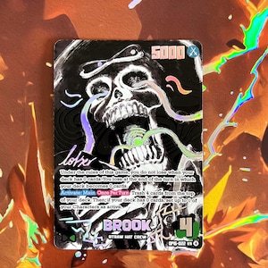 Könnte beinhalten: Holografische Sammelkarte mit einem Totenkopf mit Zylinder und dem Namen "BROOK". Die Karte zeigt die Zahl "4" und den Text "STRAW HAT CREW". Sie enthält auch die Zahl "5000" und Spielanweisungen.