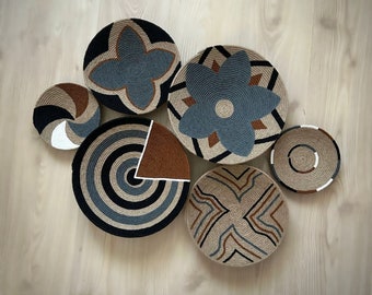 Peut inclure: Six décorations murales tissées dans différents motifs géométriques. Les pièces sont faites de matériaux naturels et présentent une combinaison de couleurs brunes, bleues et blanches.
