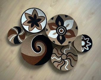 Peut inclure: Six décorations murales rondes en osier avec différents motifs en noir, blanc et marron. Les motifs comprennent une spirale, une fleur et un soleil.