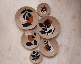 May include: Set of six woven wall decor plates with abstract designs in black, brown, and beige. The plates feature stylized plant motifs and geometric shapes.