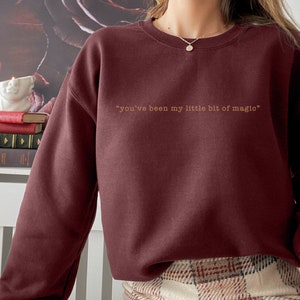 Puede incluir: Sudadera color burdeos con el texto "you've been my little bit of magic" impreso en dorado.