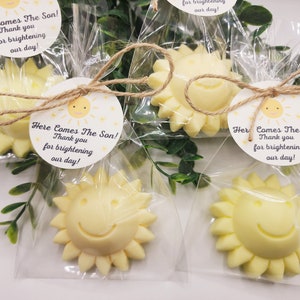 May include: Four small yellow sun-shaped favours with a smiley face are packaged in clear cellophane bags tied with twine and a small white tag that reads "Here Comes The Son! Thank you for brightening our day!"