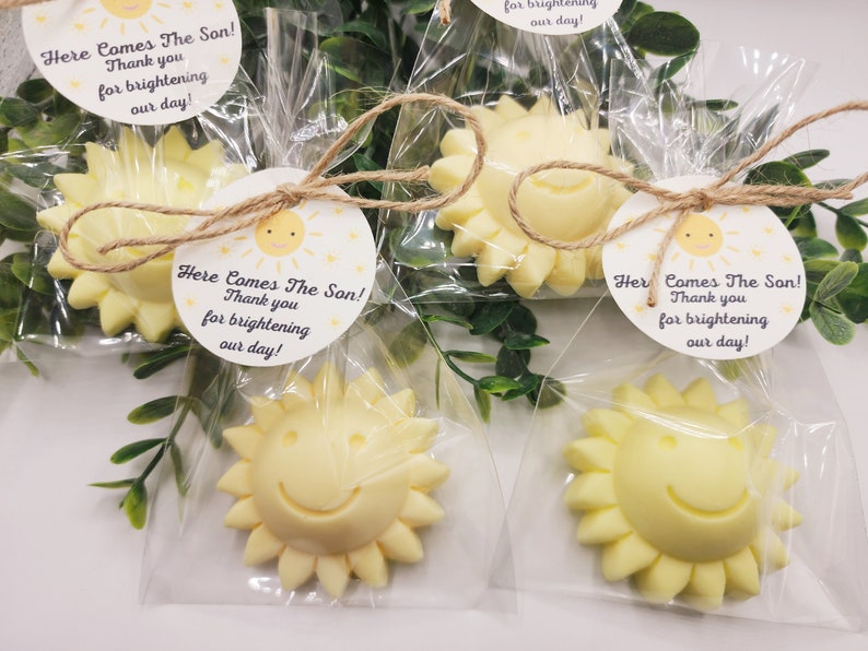 May include: Four small yellow sun-shaped favours with a smiley face are packaged in clear cellophane bags tied with twine and a small white tag that reads "Here Comes The Son! Thank you for brightening our day!"