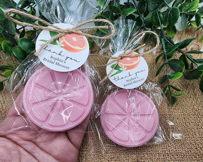 May include: Two clear cellophane bags with pink grapefruit-shaped soaps and thank you tags. The tags are round and white with a grapefruit illustration and the text "Thank you, Sophia's Bridal Shower".
