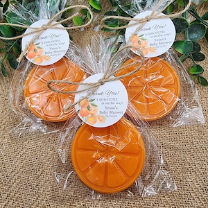 May include: Three orange-scented soap favors wrapped in cellophane bags with twine and a round tag that says "Thank You! A little cutie is on the way! Tessa's Baby Shower 06/01/24"